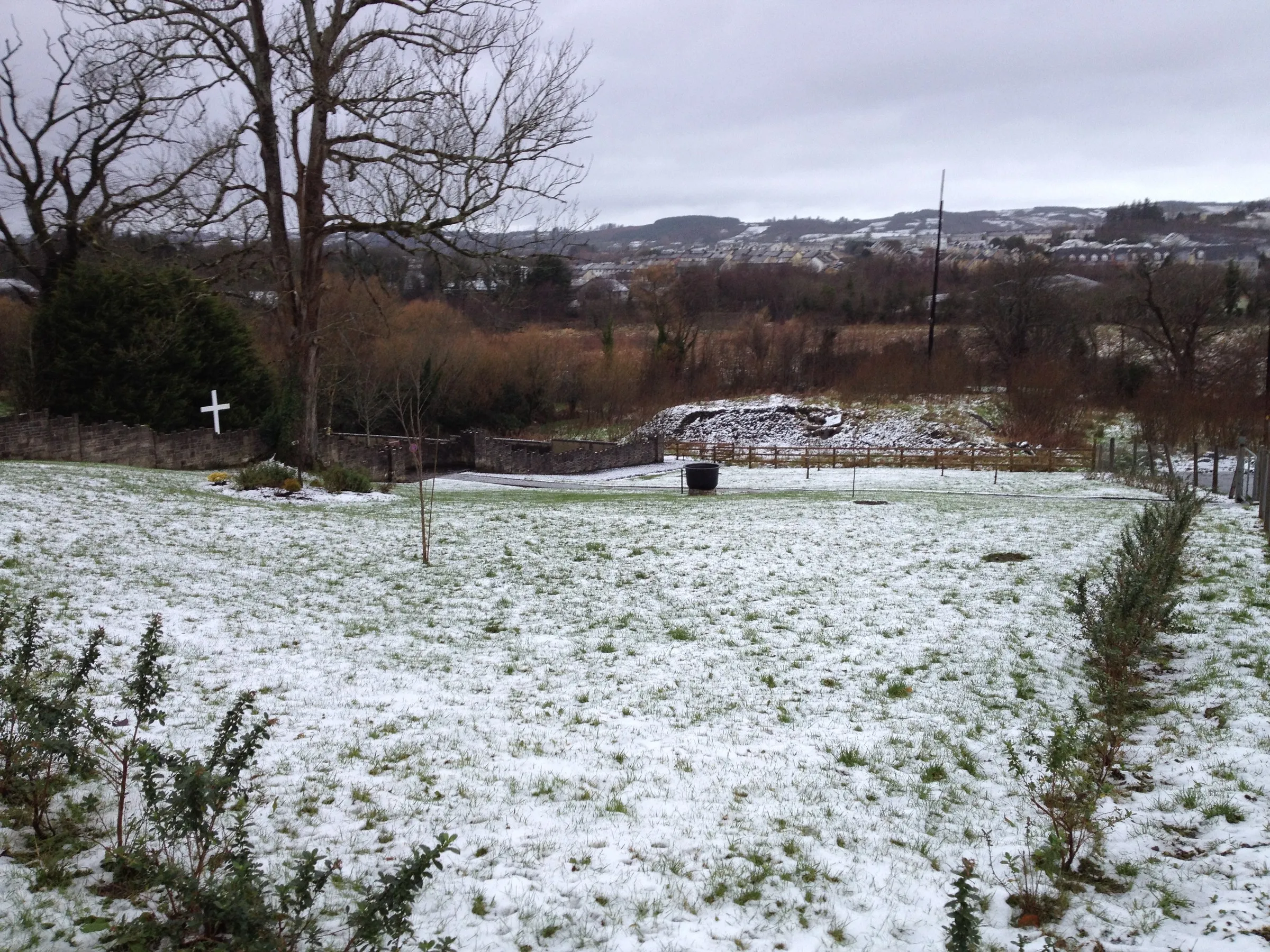 Snow lying over an empty burial field, a small cross at its edge