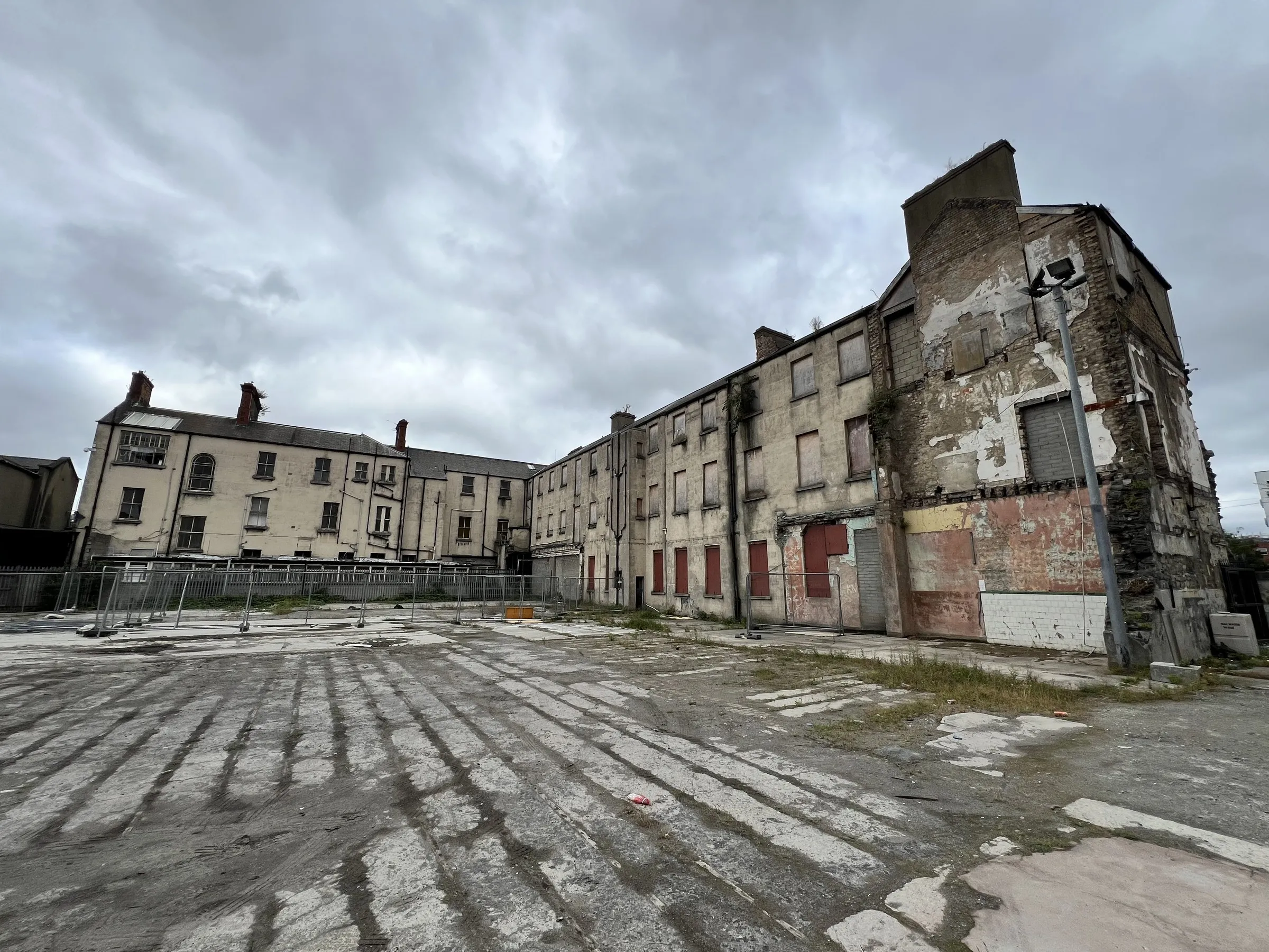 A long derelict institutional block, windows boarded, across a wet yard