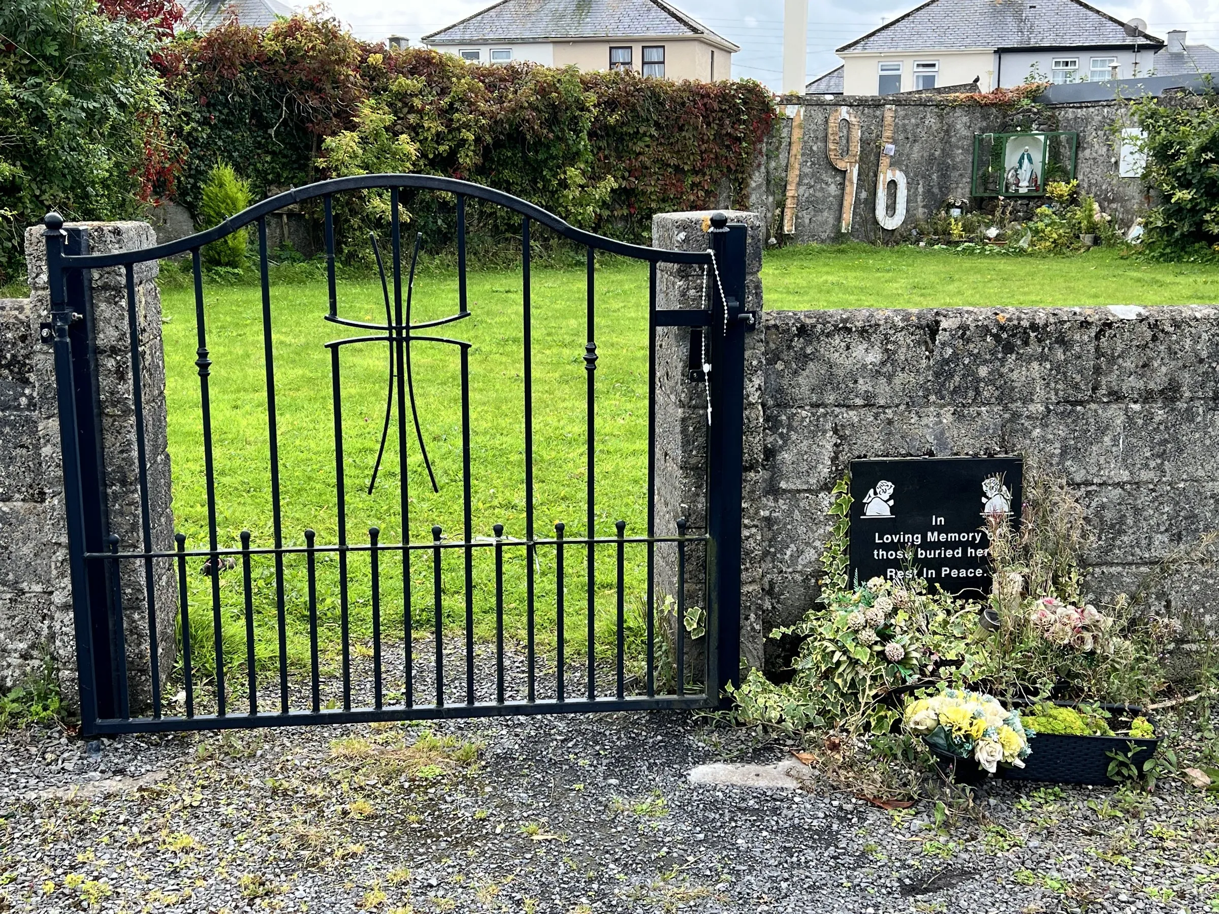 A black iron gate, a memorial plaque and flowers set into the wall beside it