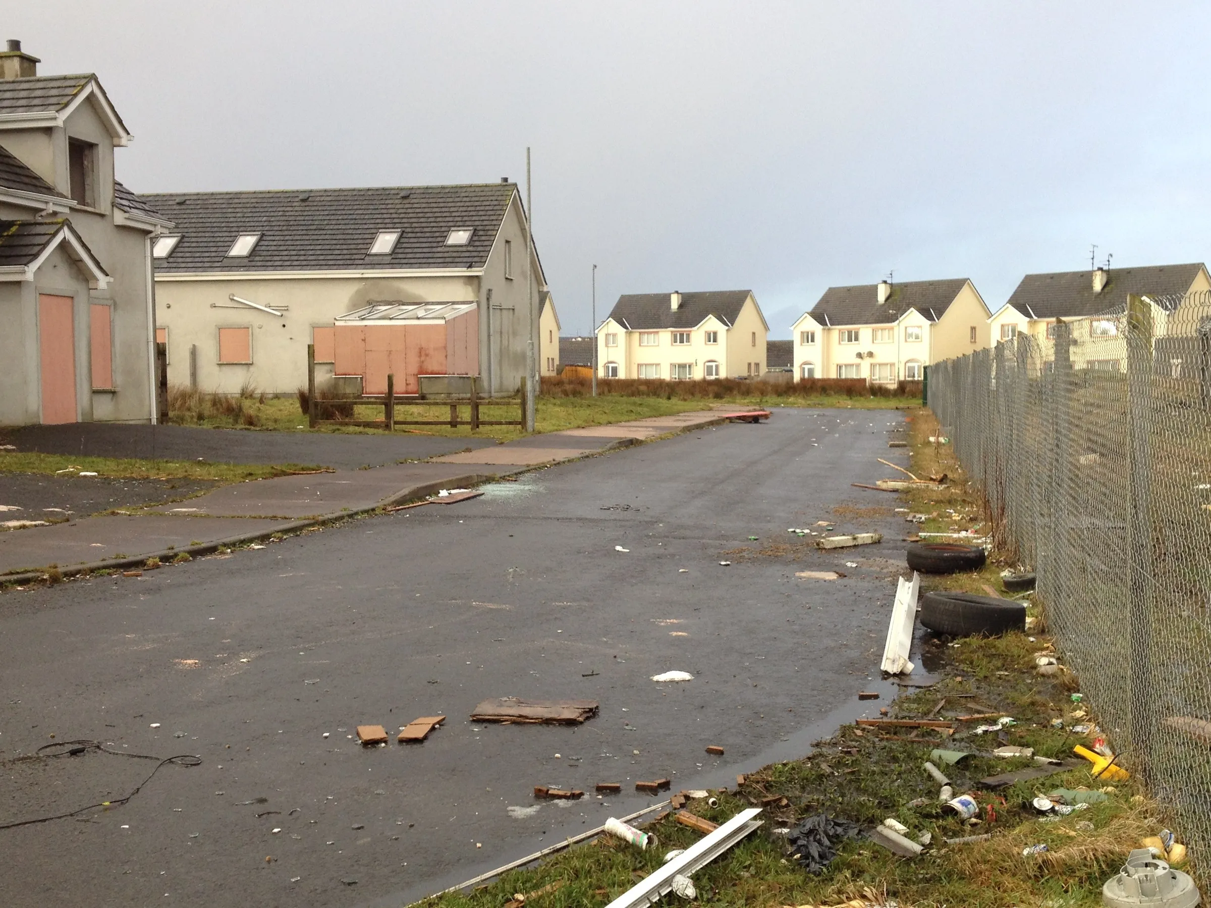 An unfinished estate road, wire fencing and scattered debris