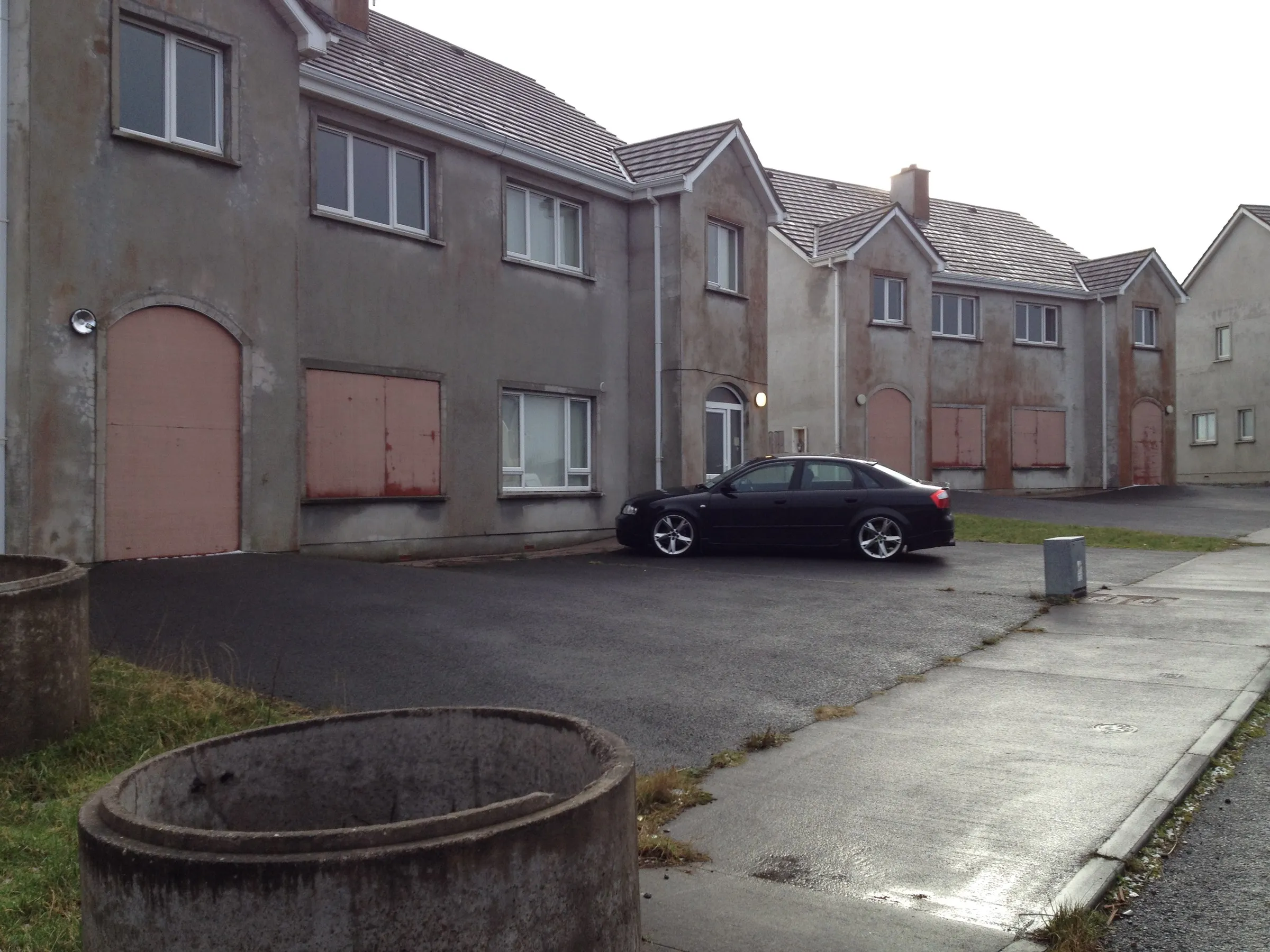 An estate street of finished houses, a concrete pipe left in the foreground