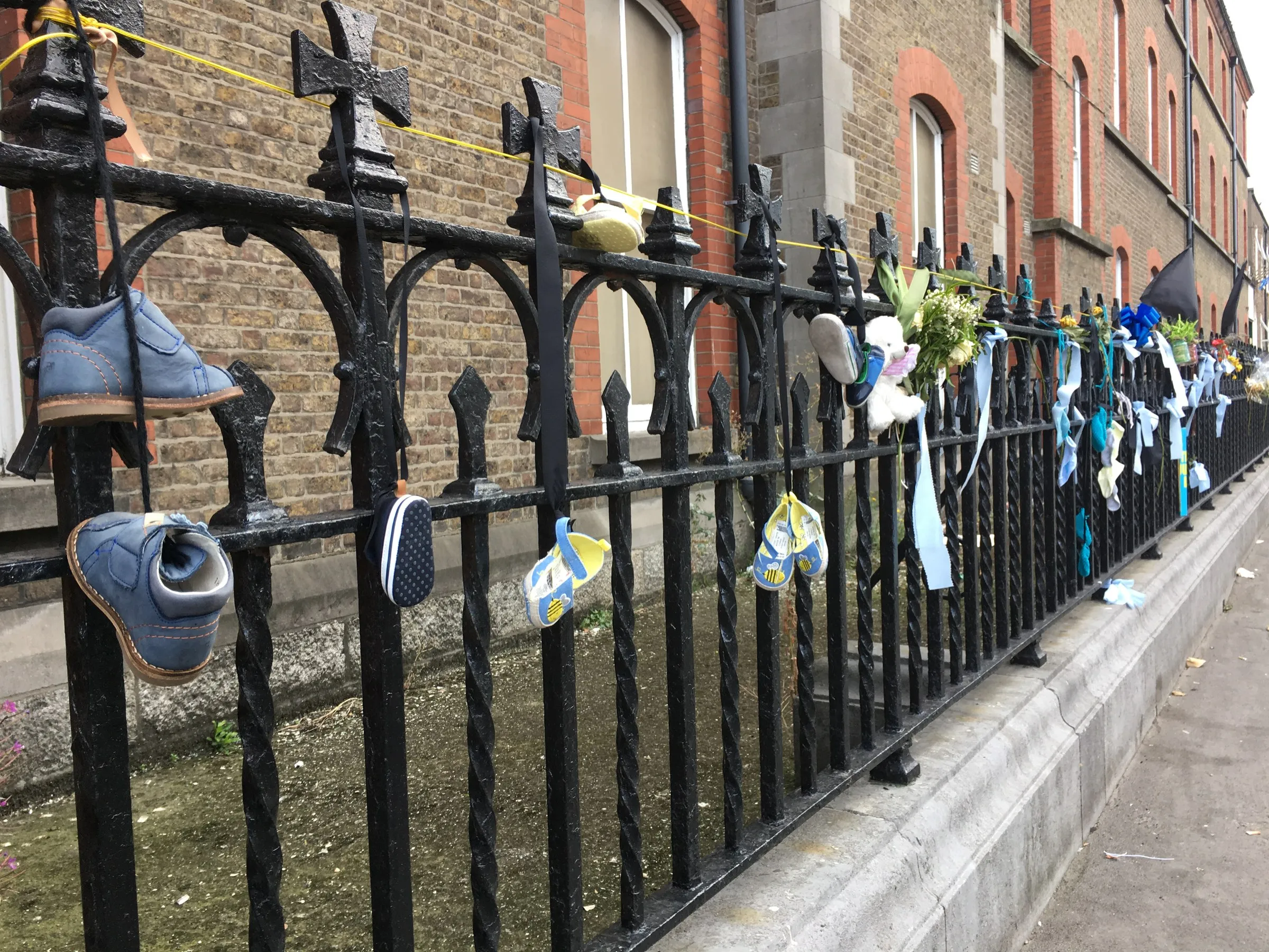 Iron railings hung the length of a street with children's shoes and ribbons
