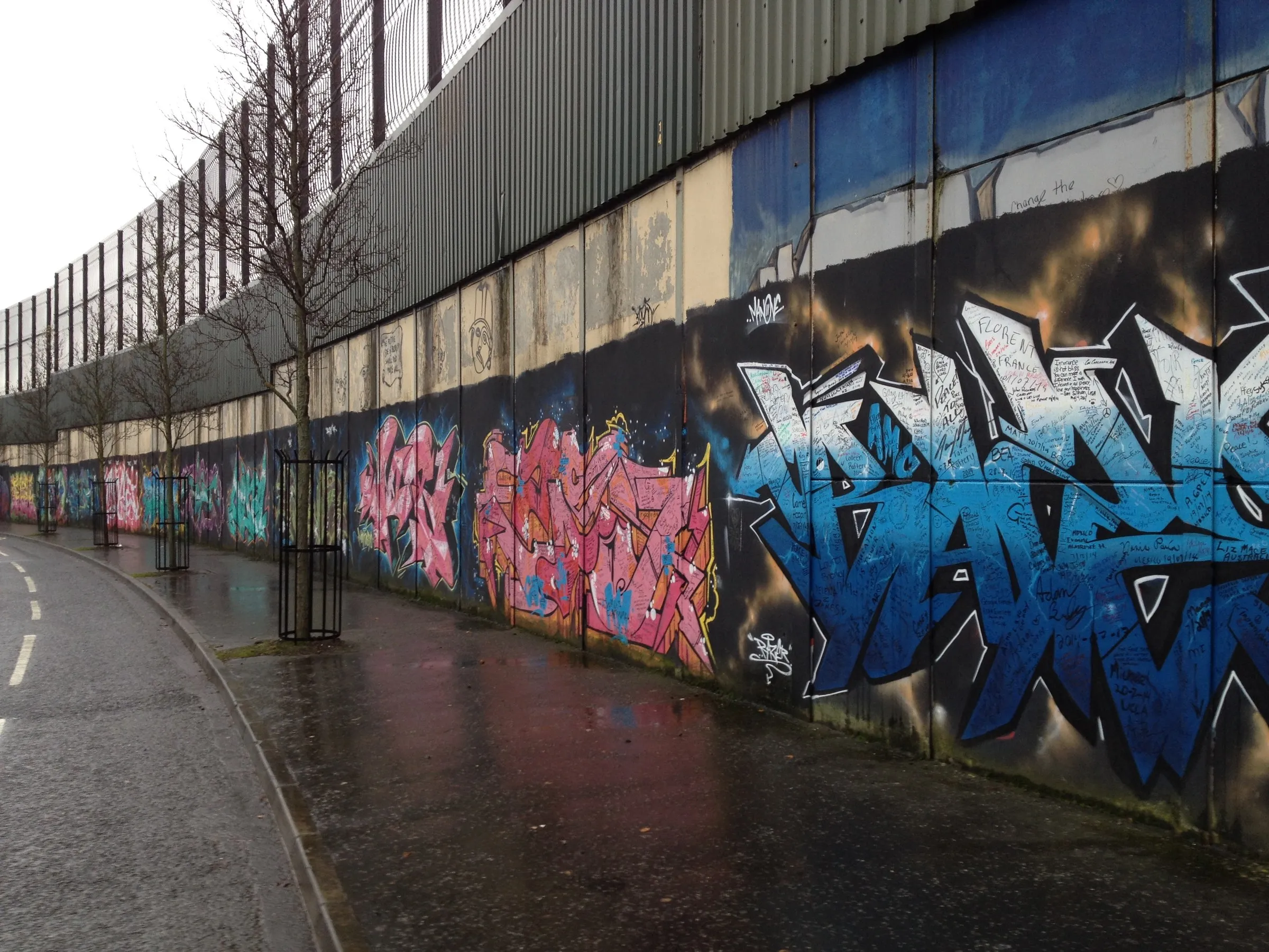 A peace wall running beside a wet road, murals along its length