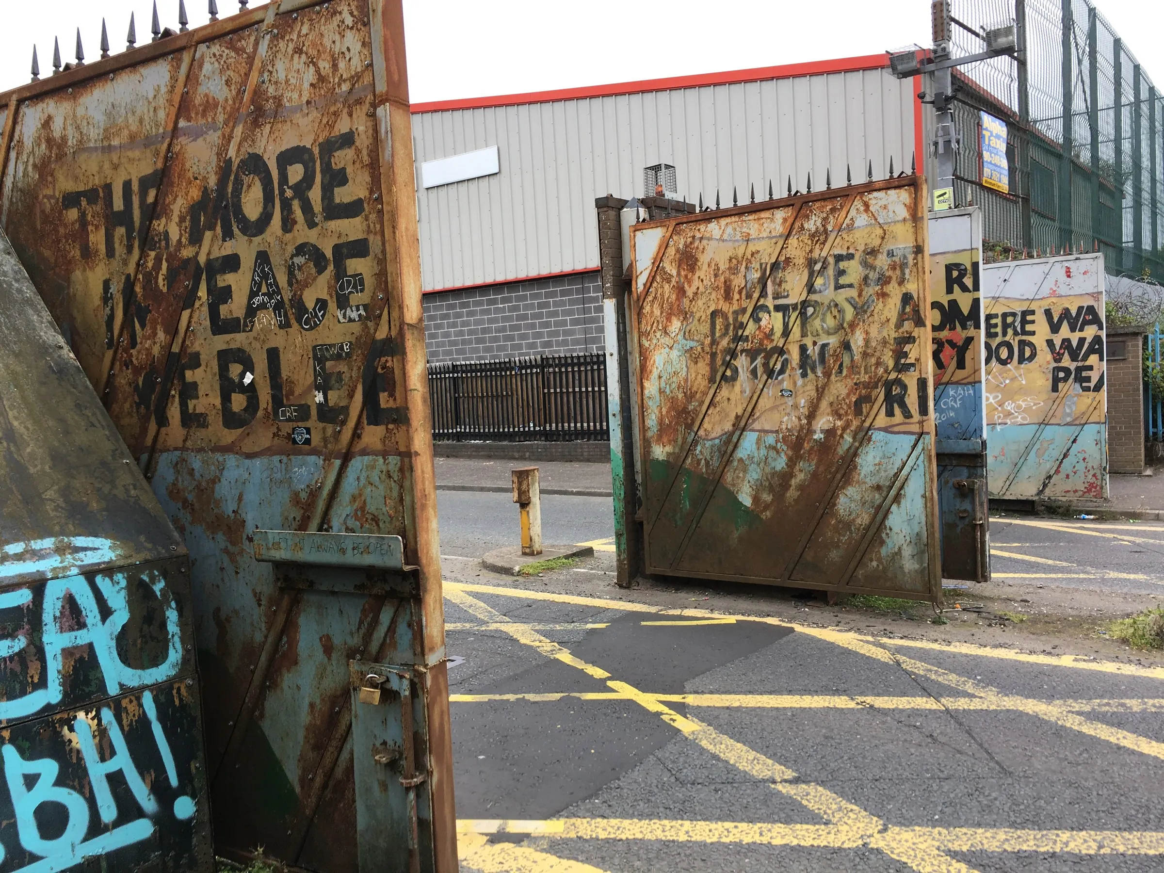 Rusted steel peace gates standing open across a road